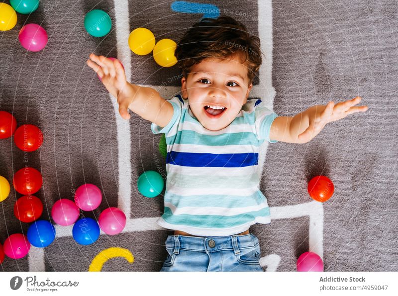 Glücklicher Junge spielt mit bunten Bällen spielen Ball werfen heimwärts Lachen lässig Stock Aktivität Spiel Himmel und Hölle aufgeregt Kind Spaß Nummer Teppich