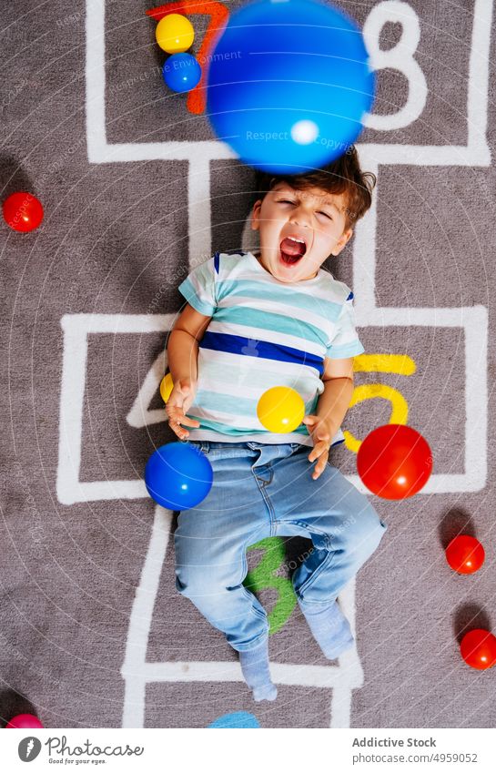 Glücklicher Junge spielt mit bunten Bällen spielen Ball werfen heimwärts Lachen lässig Stock Aktivität Spiel Himmel und Hölle aufgeregt Kind Spaß Nummer Teppich