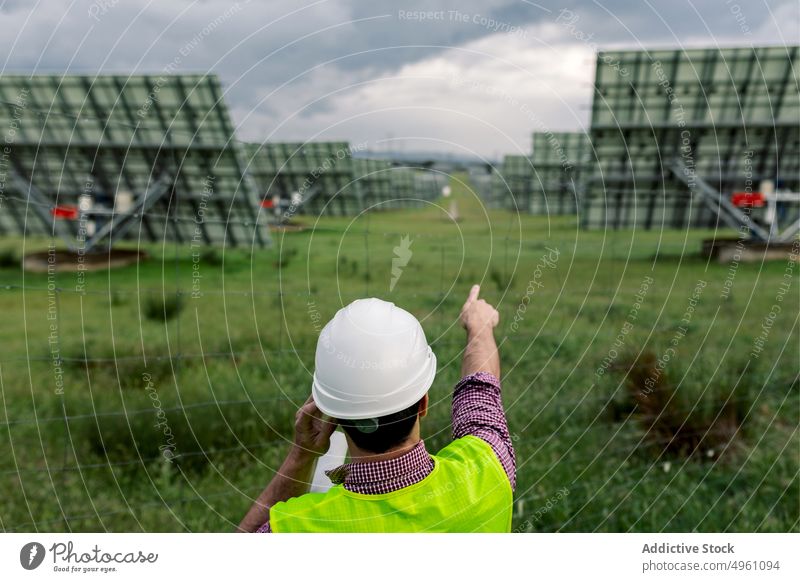 Unbekannter Techniker, der während des Telefonats auf die Photovoltaikmodule zeigt Mann Smartphone sprechen Punkt diskutieren Station Kraft Arbeit männlich