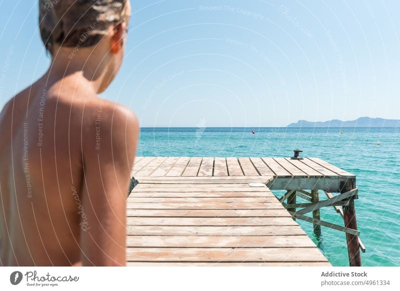 Junge steht im Sommer auf einem Holzsteg Pier MEER Teenager Feiertag sonnig nasses Haar Wochenende Urlaub Wasser blau hölzern Kai stehen nackter Torso