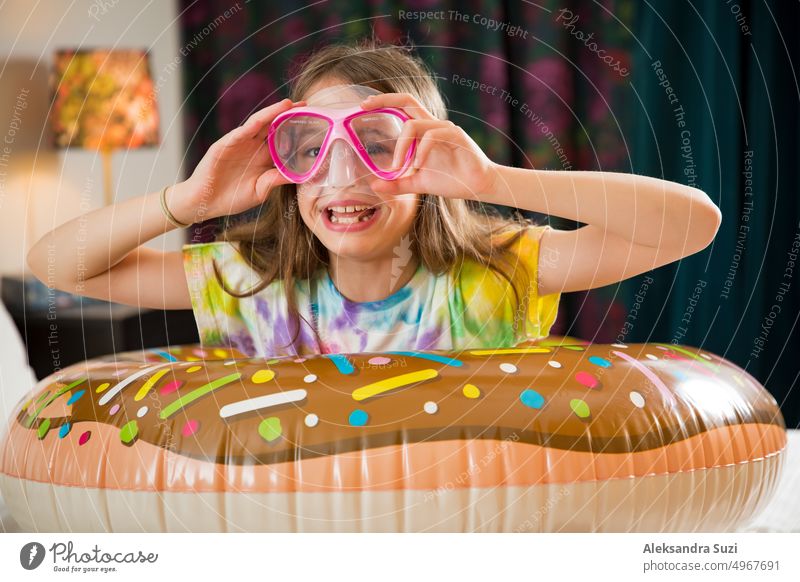 Niedliches Kind mit aufblasbarem Schwimmring und Tauchmaske auf dem Bett im Hotelzimmer sitzend. Spielend, lachend, lächelnd. Glückliche Familie Urlaub. Strand