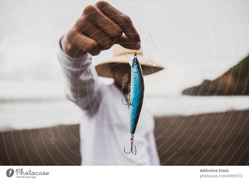 Unbekannter Angler mit Stecker in der Hand Fischer blau Fischen anpacken ködern Küste Ufer Vorrat Hobby Gerät vorbereiten männlich Meeresufer Seeküste Hut