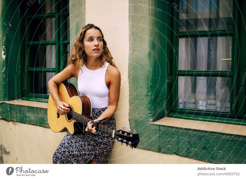 Lockige Frau spielt Gitarre und lehnt sich an die Wand Musik Spielen romantisch jung spielen Instrument heiter Musical Spaß Urlaub Mode Feiertag lässig Sommer