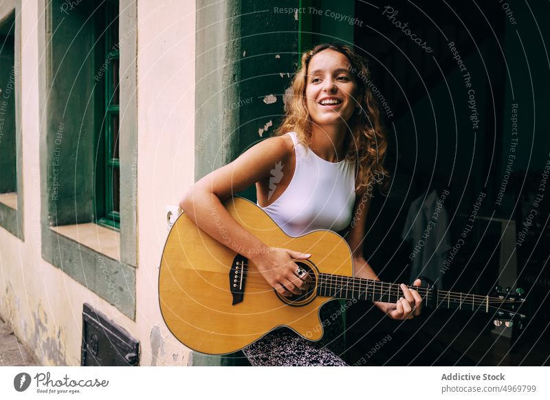 Lockige, Gitarre spielende Frau, die in einem Fenster sitzt Musik Spielen romantisch jung Instrument heiter Musical Spaß Urlaub Mode Feiertag lässig Sommer