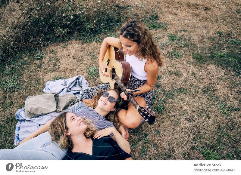 Frau lächelt und spielt Gitarre für Freunde auf einem Feld Spielen genießend hören jung spielen romantisch Instrument Freundschaft heiter Partnerschaft