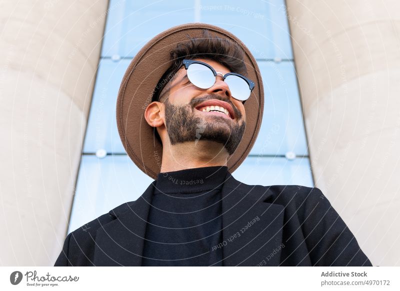 Maskuliner Mann mit trendiger Sonnenbrille hinter einem Geländer in der Stadt Mode Stil Individualität kreativ Design Zeitgenosse maskulin Hut Jacke Macho