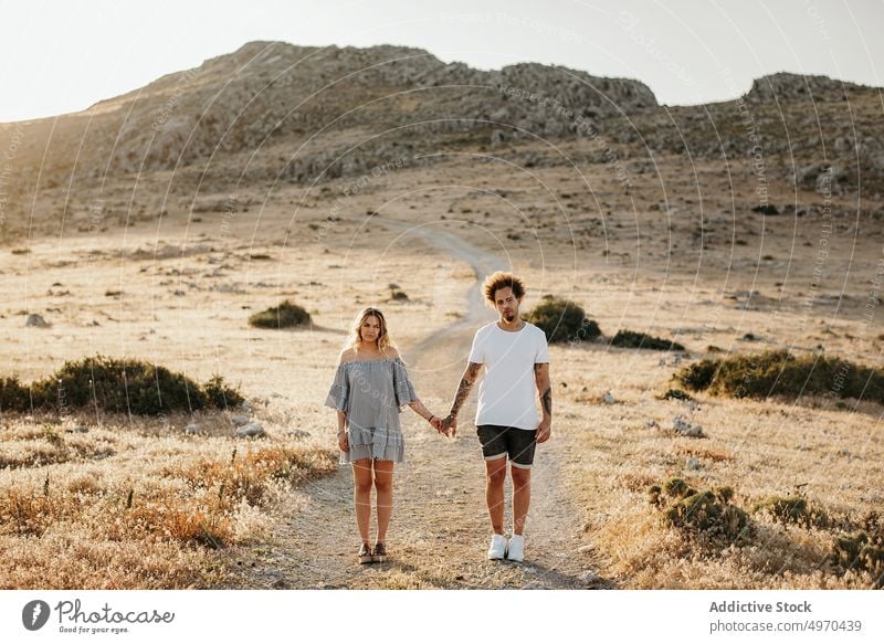 Paar, das sich an den Händen hält, während es auf einem Fußweg gegen einen felsigen Hügel am Abend steht Spaziergang romantisch schlendern Liebe ernst Freundin