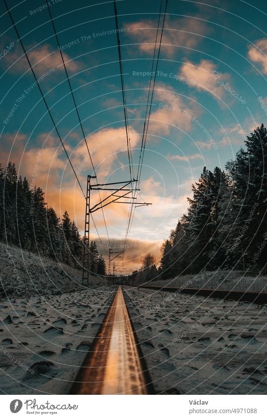 Dramatischer Sonnenuntergang auf einer schneebedeckten Eisenbahnstrecke während eines strengen Winters in Kajaani, Region Kainu, Finnland Zug kajaani