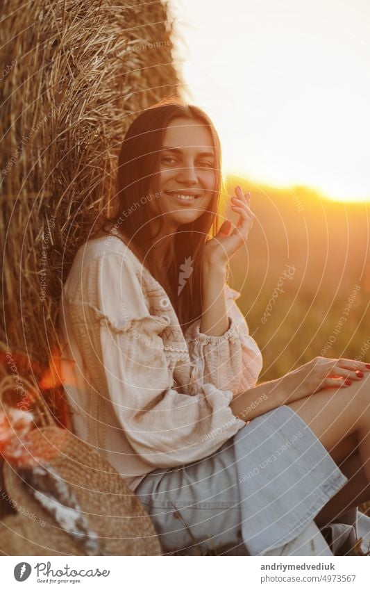 Junge Frau im schönen Licht des Sommers Sonnenuntergang in einem Feld sitzt in der Nähe der Strohballen. schöne romantische Mädchen mit langen Haaren im Freien im Feld