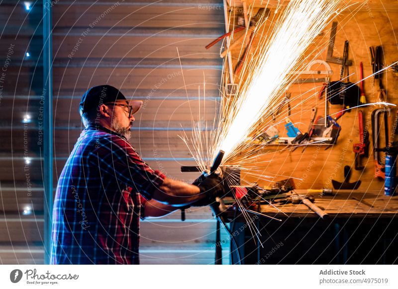 Mann schneidet ein Stück Metall in einer modernen Werkstatt Winkelschleifer Funken Arbeiter Gerät benutzend Arbeitsplatz Instrument Mechaniker Kunsthandwerker