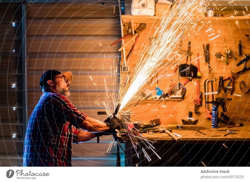 Mann schneidet ein Stück Metall in einer modernen Werkstatt Winkelschleifer Funken Arbeiter Gerät benutzend Arbeitsplatz Instrument Mechaniker Kunsthandwerker