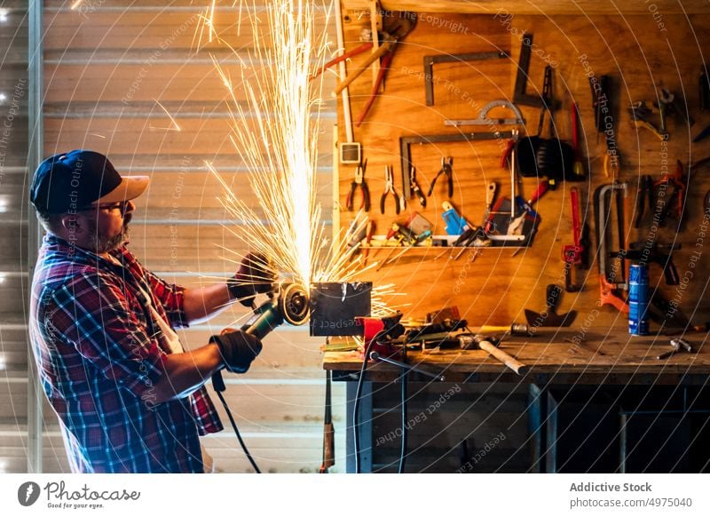 Mann schneidet ein Stück Metall in einer modernen Werkstatt Winkelschleifer Funken Arbeiter Gerät benutzend Arbeitsplatz Instrument Mechaniker Kunsthandwerker