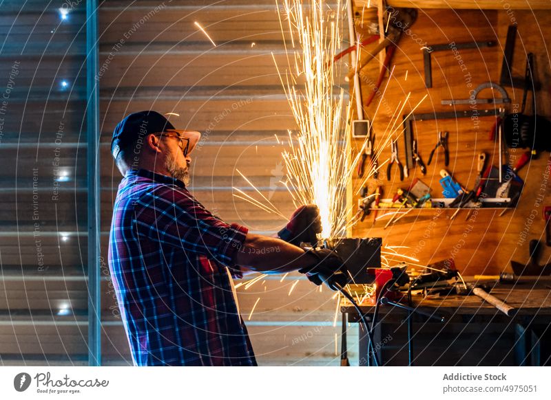 Mann schneidet ein Stück Metall in einer modernen Werkstatt Winkelschleifer Funken Arbeiter Gerät benutzend Arbeitsplatz Instrument Mechaniker Kunsthandwerker