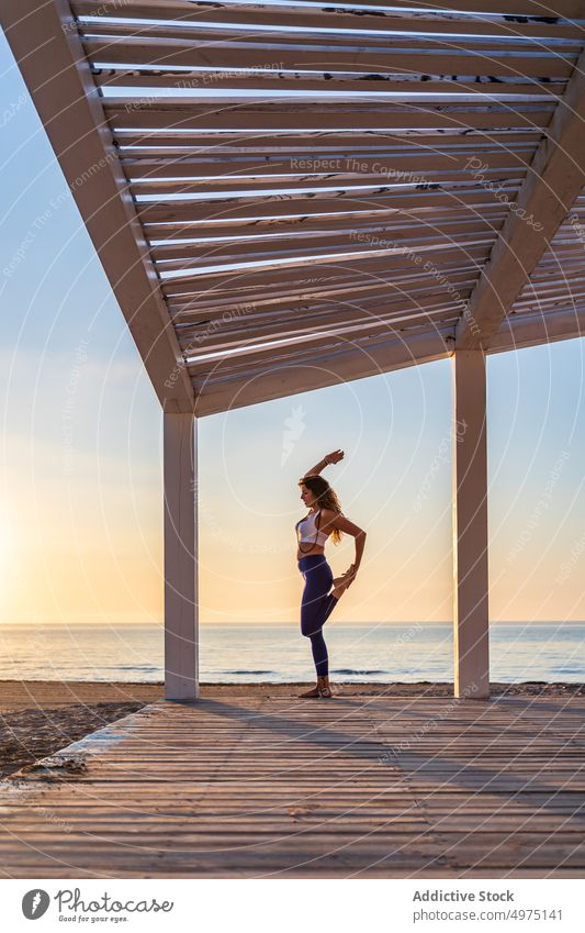 Frau macht Yoga in stehender geteilter Pose am Meer Stehende Teilung Gleichgewicht beweglich Sportbekleidung Split Meeresufer Sonnenaufgang üben Gesundheit