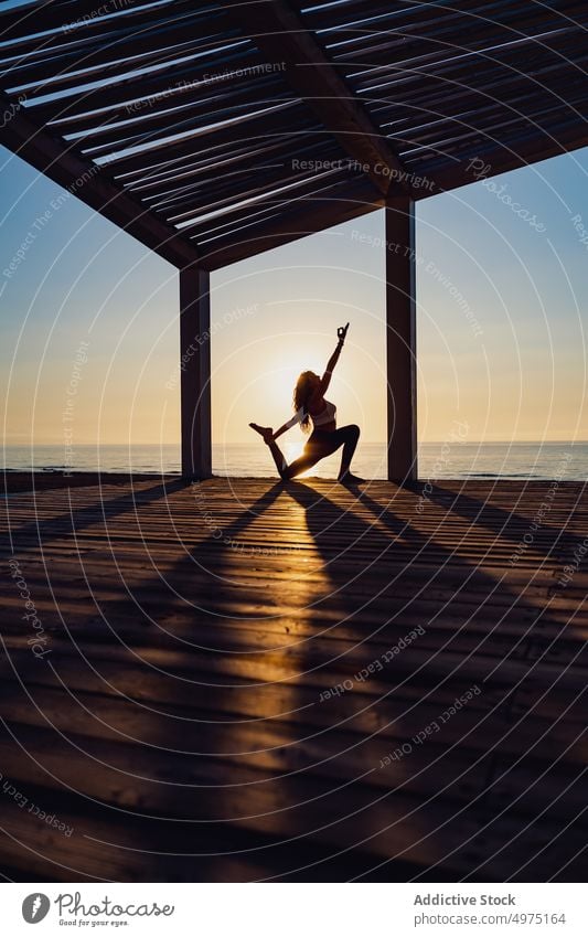 Ruhige Frau macht Yoga in Kriegerpose bei Sonnenaufgang Pose Seeküste üben ruhig Silhouette Morgendämmerung hölzern Terrasse MEER Gesundheit Harmonie