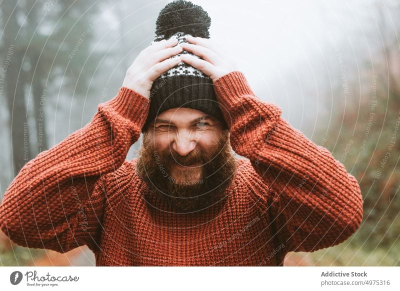 Bärtiger Mann in Pullover und Hut in der Nähe von Tannenbäumen Wald Regen Mantel Baum kalt Wetter Wasser Tropfen regnerisch bärtig nachdenklich Holz Denken Typ