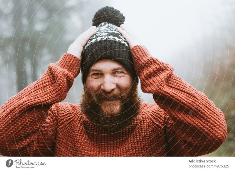 Bärtiger Mann in Pullover und Hut in der Nähe von Tannenbäumen Wald Regen Mantel Baum kalt Wetter Wasser Tropfen regnerisch bärtig nachdenklich Holz Denken Typ