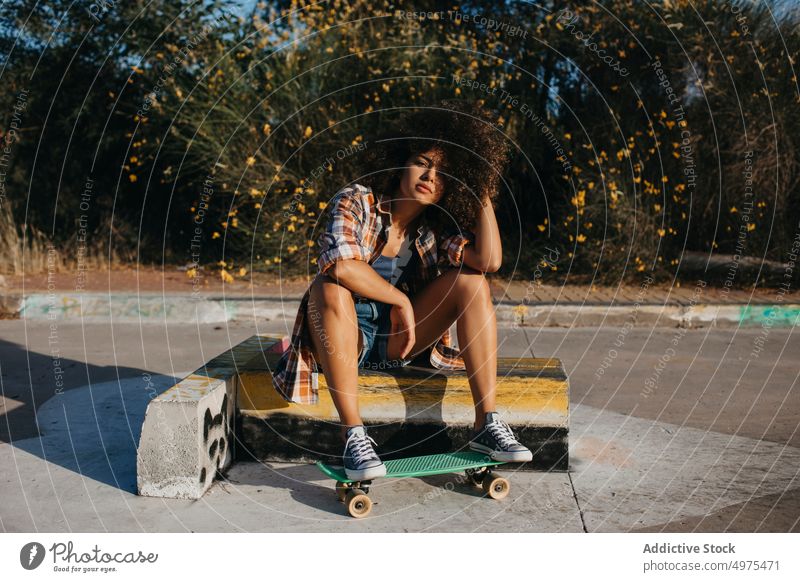 Ruhige afroamerikanische Frau mit Penny Board auf der Straße Lochrasterplatte Sommer Skater cool tausendjährig Afro-Look trendy ruhig Hipster sonnig ethnisch