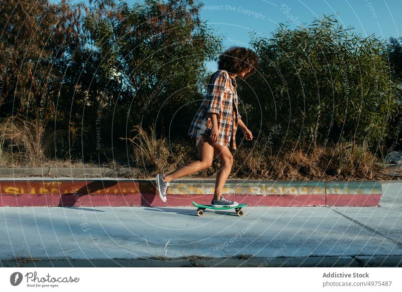 Ethnische Frau reitet Penny Board Lochrasterplatte Mitfahrgelegenheit Sonnenuntergang Straße Sommer Hipster Skater Afro-Look urban ethnisch trendy ruhig