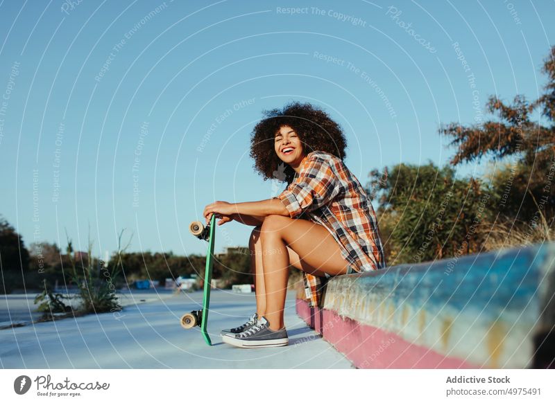 Ruhige afroamerikanische Frau mit Penny Board auf der Straße Lochrasterplatte Sommer Skater cool tausendjährig Afro-Look trendy ruhig Hipster sonnig ethnisch