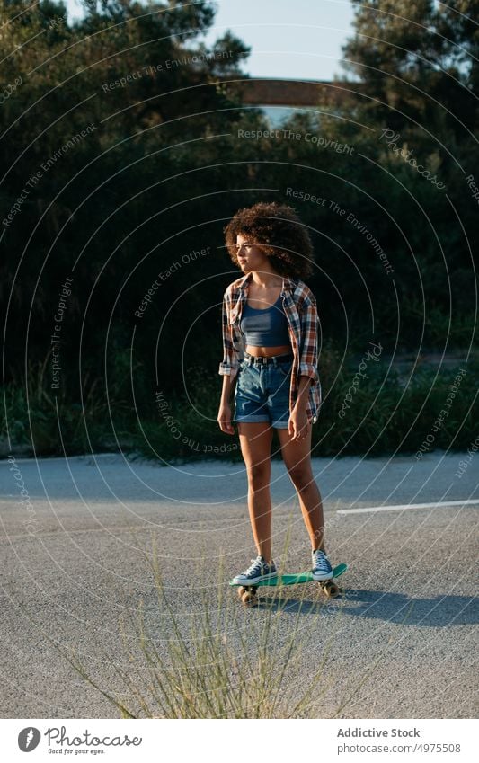 Ethnische Frau reitet Penny Board Lochrasterplatte Mitfahrgelegenheit Sonnenuntergang Straße Sommer Hipster Skater Afro-Look urban ethnisch trendy ruhig