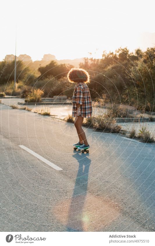 Ethnische Frau reitet Penny Board Lochrasterplatte Mitfahrgelegenheit Sonnenuntergang Straße Sommer Hipster Skater Afro-Look urban ethnisch trendy ruhig