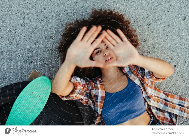 Eine afroamerikanische Frau liegt mit einem Brett auf der asphaltierten Straße Lochrasterplatte Sommer Skater tausendjährig Afro-Look Asphalt trendy ruhig