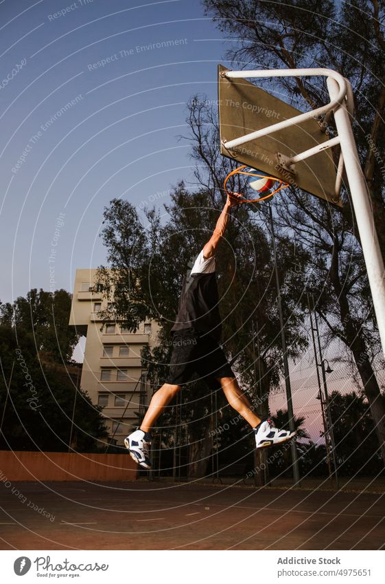 Starker entschlossener Mann, der nachts auf dem Platz Basketball spielt eintauchen Korb Nacht Park Ball springen Schuss Reifen werfen Sportpark Gericht Spiel