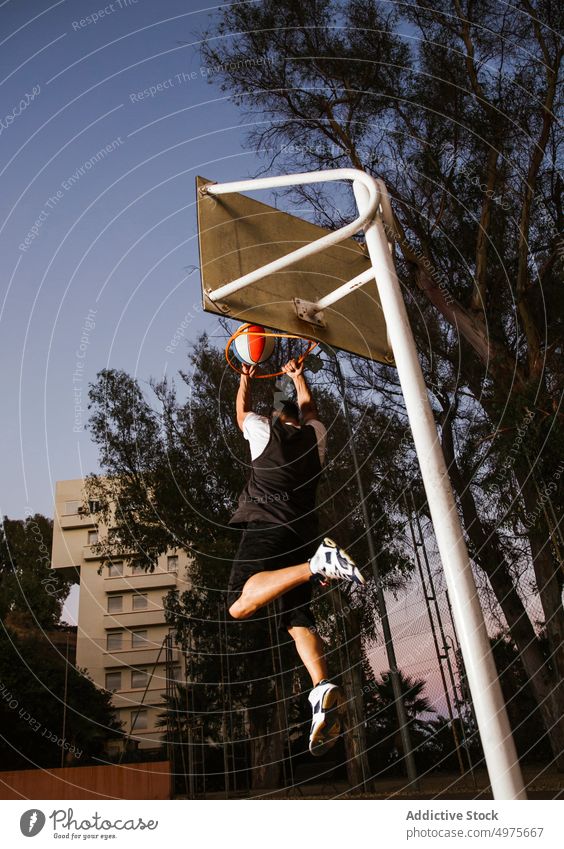 Starker entschlossener Mann, der nachts auf dem Platz Basketball spielt eintauchen Korb Nacht Park Ball springen Schuss Reifen werfen Sportpark Gericht Spiel