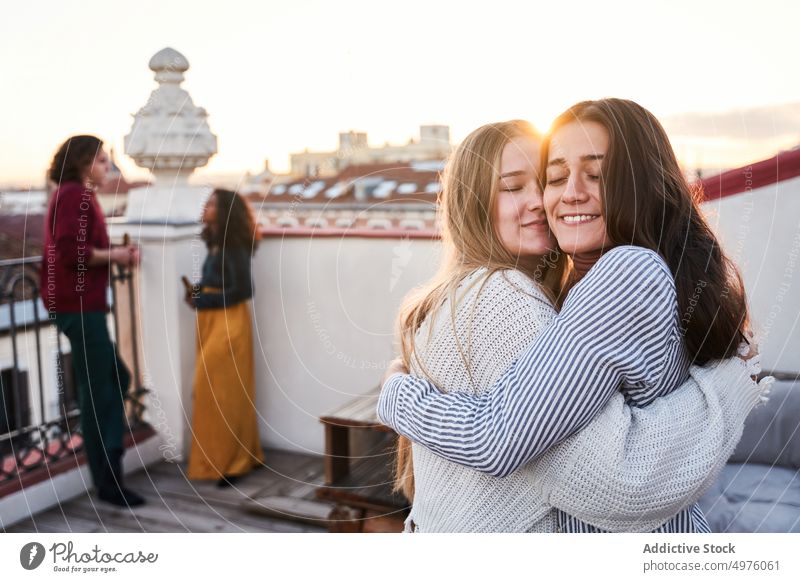 Fröhliche Frauen umarmen sich auf der Terrasse während einer Party Freund Umarmung Zahnfarbenes Lächeln freudig Dachterrasse Umarmen heiter Treffpunkt