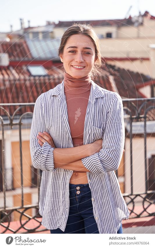 Lächelnde Frau, die mit verschränkten Armen auf dem Dach eines Gebäudes steht heiter Zahnfarbenes Lächeln verschränkte Arme Dachterrasse Terrasse Inhalt Stadt