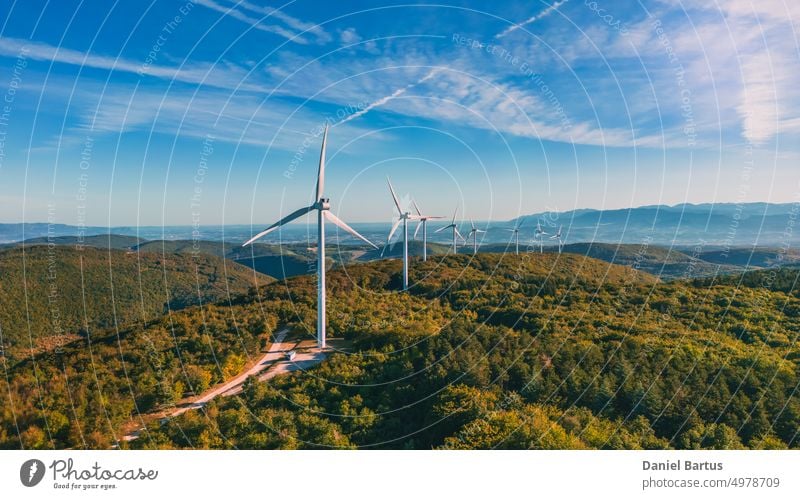 Blick auf einen Windpark in einem bergigen Waldgebiet mit Bergen im Hintergrund. Blick bei aufgehender Sonne. Sonnenaufgang. alternativ blau elektrisch