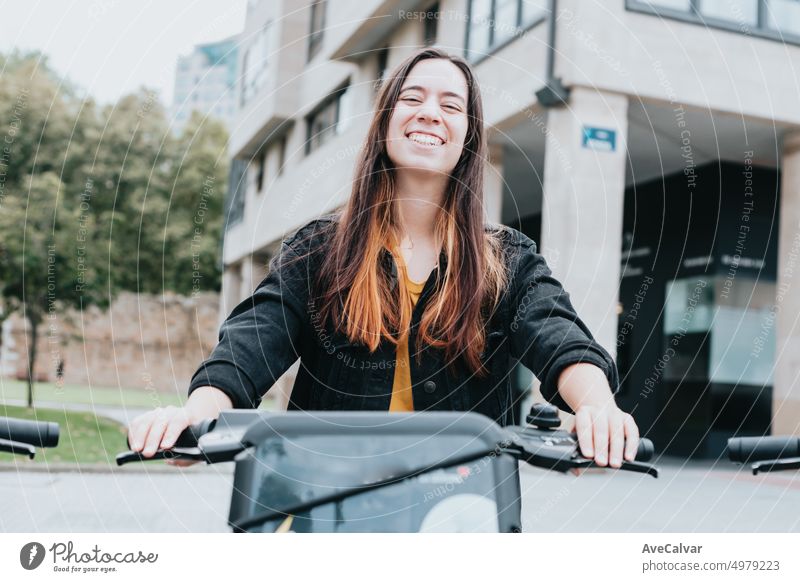 Porträt eines jungen Erwachsenen, der ein Elektrofahrrad mietet, um die Stadt zu besichtigen.Verschiedene Möglichkeiten, sich fortzubewegen und touristische Planungen vorzunehmen.Städtische, ökologische und öffentliche Verkehrsmittel.Fröhliche, lächelnde und aufgeregte Frau