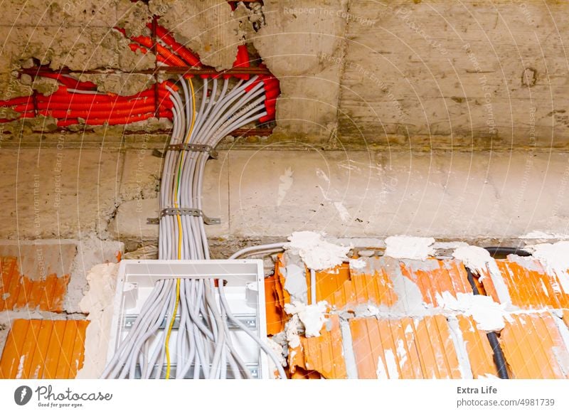 Ein Kabelstapel hängt an einem Sicherungskasten, der an der Wand eines unfertigen Gebäudes angebracht ist. Klotz Kasten Baustein Baustelle Bündel Schaltkreis