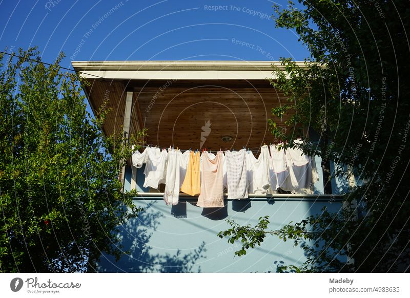 Wäscheleine mit frisch gewaschener Wäsche und Unterwäsche auf dem Balkon und der Veranda eines alten Wohnhaus vor blauem Himmel im Sonnenschein in Adapazari in der Provinz Sakarya in der Türkei