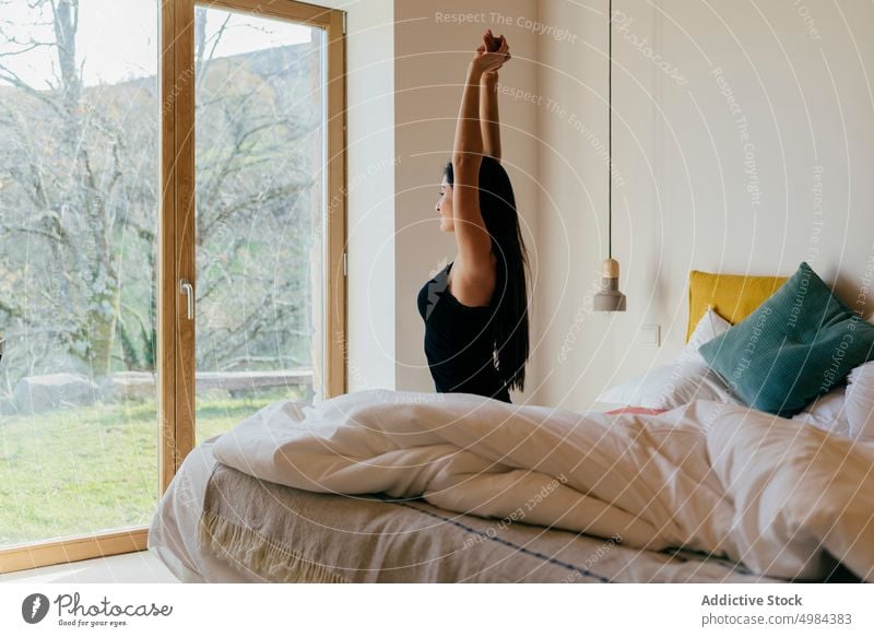 Charmante hispanische Dame mit erhobenen Händen auf dem Bett in der Nähe des Fensters Schlafzimmer erhöht Hand charmant Frau Raum attraktiv jung schön schlank