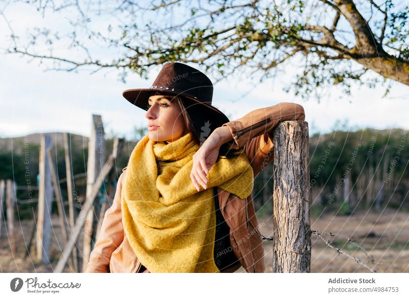 Stilvolle Frau mit Schal und Cowboyhut schön Ranch Natur Stehen Hut Cowgirl trendy nachdenklich träumend brünett Harmonie Zaun jung Landschaft Holz Lehnen