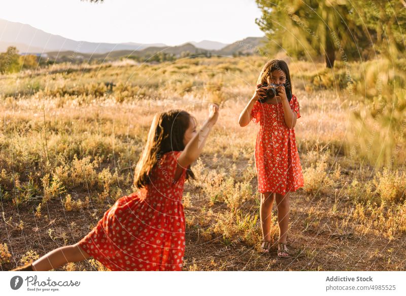 Mädchen, das seine kleine Schwester auf einer Wiese fotografiert Freundschaft fotografierend Sommer Feld Natur Fotokamera Fotografie Glück schön