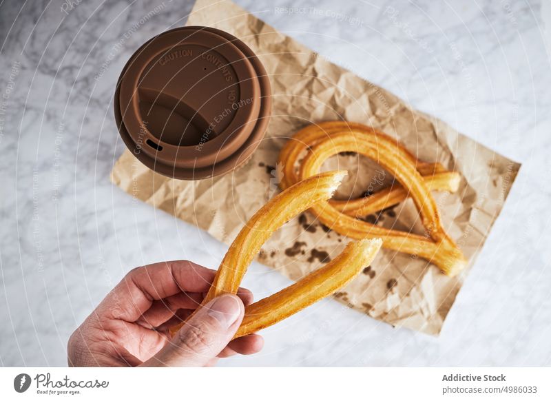 Crop-Person isst Churros zum Frühstück essen Kaffee Snack Tasse Morgen Amuse-Gueule Getränk trinken Lebensmittel Tisch lecker frisch Mahlzeit Becher heimwärts