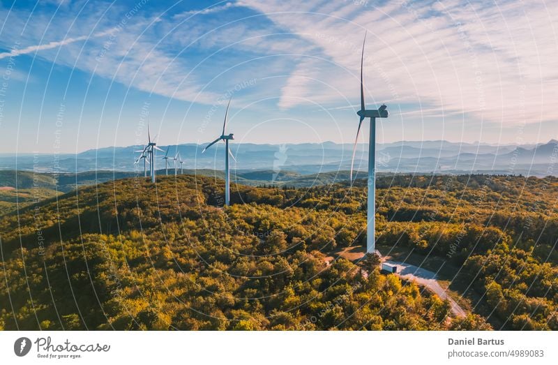 Blick auf einen Windpark in einem bergigen Waldgebiet mit Bergen im Hintergrund. Blick bei aufgehender Sonne. Sonnenaufgang Berge u. Gebirge Bauernhof Energie