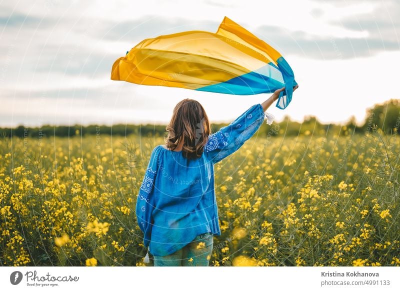 Ukrainische Patriotin schwenkt Nationalflagge im rapsgelben Feld. Selten, Rückenansicht. Ukraine unzerbrechlich, Frieden, Unabhängigkeit, Freiheit, Sieg im Krieg.