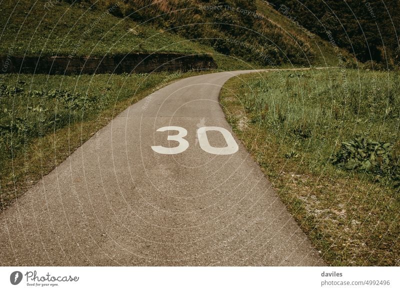 Ein Radweg, der durch die Landschaft führt, mit einer weißen Nummer 30 auf dem Asphalt. Tempo 30 Gasse Alpen Fahrrad Fahrradweg Zyklus Stock Fußweg Gras grün