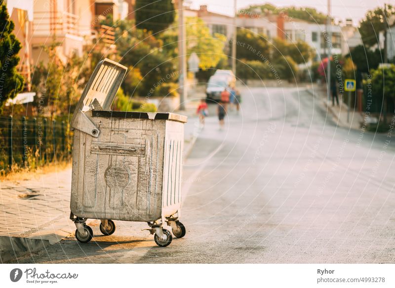 Metallabfallbehälter auf Rädern auf der Straße im Sommer an einem sonnigen Abend. Container für die vorübergehende Lagerung von Abfällen. Abfalleimer, Mülltonne, Mülleimer