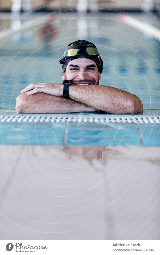 Lächelnder Schwimmer mit Schwimmbrille, der sich an den Beckenrand lehnt sich auf die Hand lehnen herzlich Schutzbrille freundlich maskulin Mann Porträt Athlet