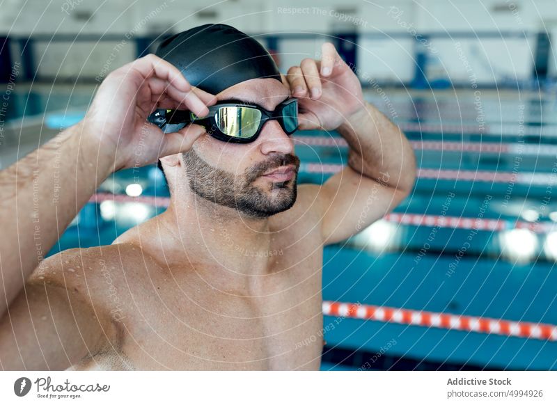 Muskulöser Schwimmer mit Schwimmbrille und Kappe am Pool Athlet Schutzbrille sportlich maskulin Macho Mann Porträt brutal Trizeps ohne Hemd Muskel Accessoire