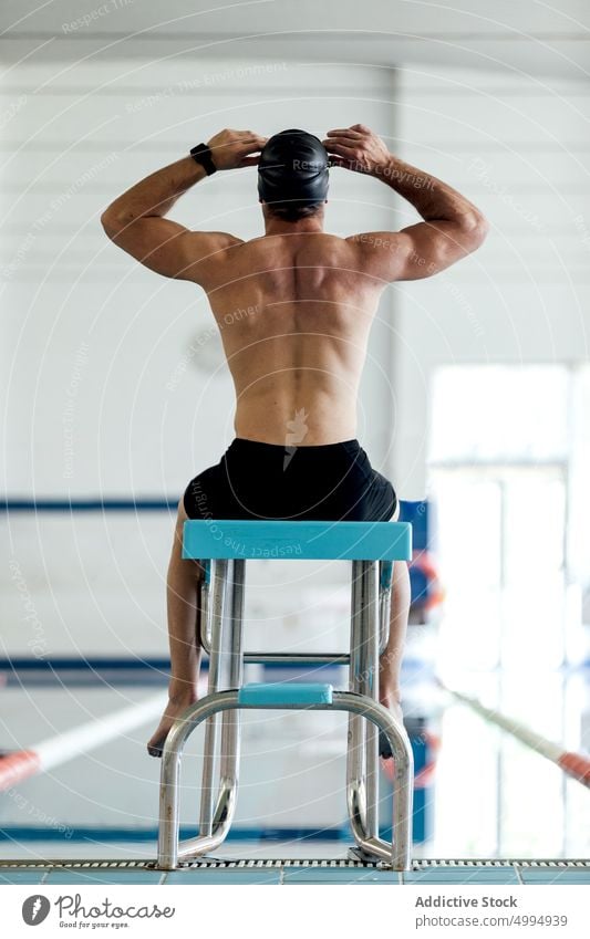 Nicht erkennbarer muskulöser Sportler, der auf einem Block am Pool sitzt Training Schwimmsport Klotz Mann Schwimmer Podest vorbereiten professionell