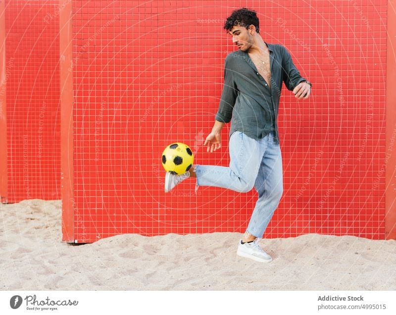 Hispanischer Mann macht Trick mit Fußball Ball Kick Straße Wand farbenfroh hell Aktivität üben Wochenende männlich jung hispanisch ethnisch jonglieren urban