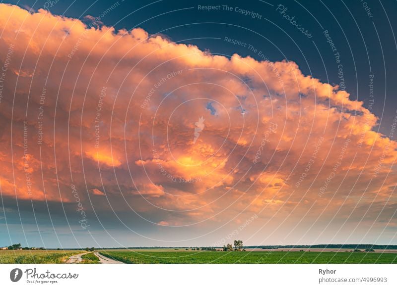 Dramatische bunten Himmel während nähert Frühlingssturm über Landschaft mit ländlichen Landstraße durch grünes Feld und Wiese im Frühsommer Saison. Pathway, Weg, offene Straße in der landwirtschaftlichen Landschaft