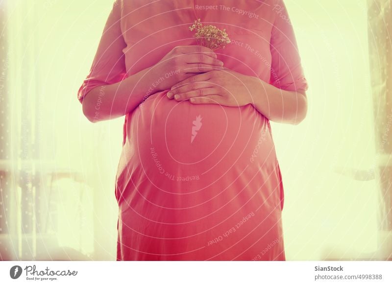 Nahaufnahme des Bauches einer schwangeren Frau, die einen Blumenstrauß in den Händen hält Schwangerschaft erwartend Mutter Mutterschaft Liebe Baby weiß