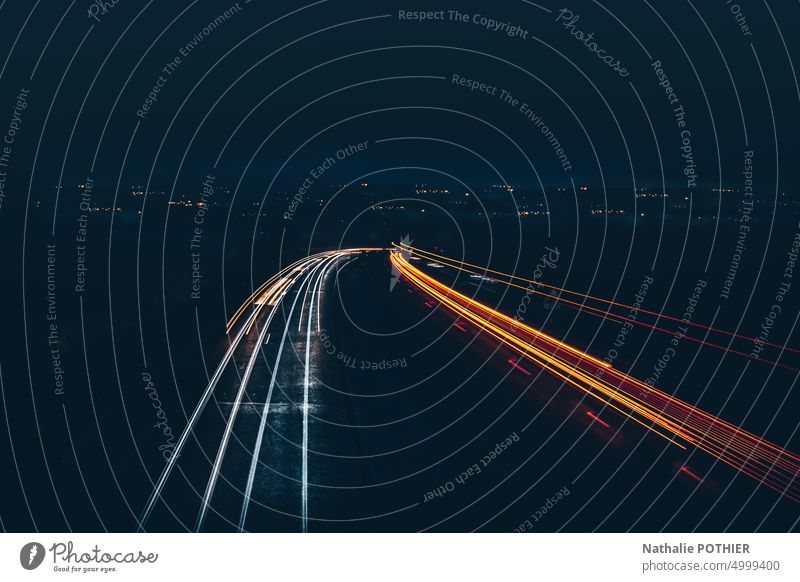 Autobahn bei Nacht mit Stadtbeleuchtung in der Ferne Licht schwarz dunkel Langzeitbelichtung Nachtaufnahme Linie Außenaufnahme Geschwindigkeit Bewegung gelb PKW